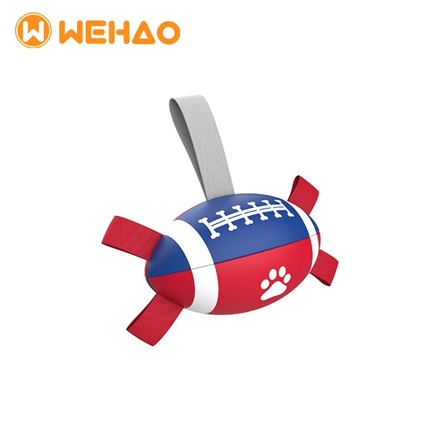 Red, white, and blue football shaped dog tug toy featuring a paw print, bone laces, and heavy-duty nylon straps for interactive fetch.